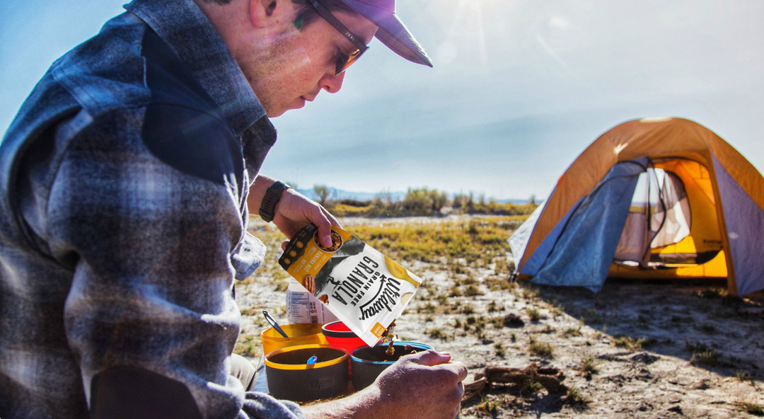 A man camping with a tent in the background pouring Wildway Banana Nut Granola into a bowl